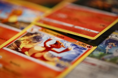 A close-up shot of various Pokémon trading cards laid out, with the focus on a Charmander card. The cards have vibrant and colorful illustrations featuring Pokémon characters and associated game stats.