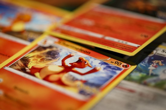 A close-up shot of various Pokémon trading cards laid out, with the focus on a Charmander card. The cards have vibrant and colorful illustrations featuring Pokémon characters and associated game stats.
