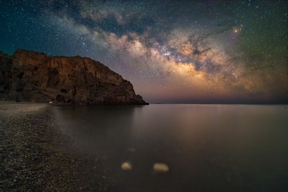 a body of water with a rocky cliff and stars in the sky