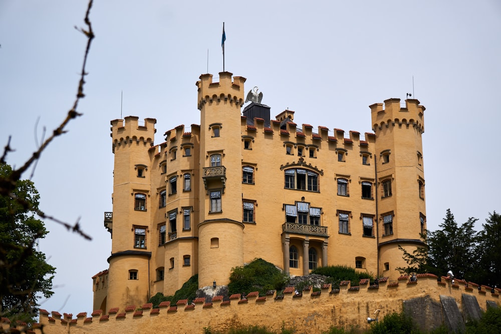 a large building with a flag on top with Hohenschwangau Castle in the background