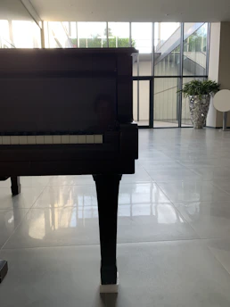 A grand piano bathed in soft natural light beside a window with delicate white curtains, evoking a serene wedding atmosphere.