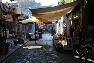 A sunlit cobblestone street lined with colorful market stalls and lively travelers enjoying a sunny afternoon.