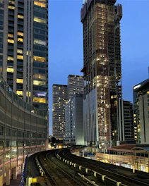 A vibrant cityscape with a train passing by modern hotels and bright lights at dusk.