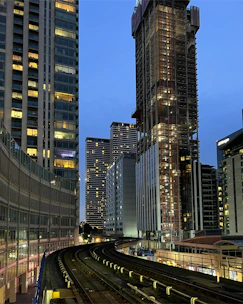 A vibrant cityscape with a train passing by modern hotels and bright lights at dusk.