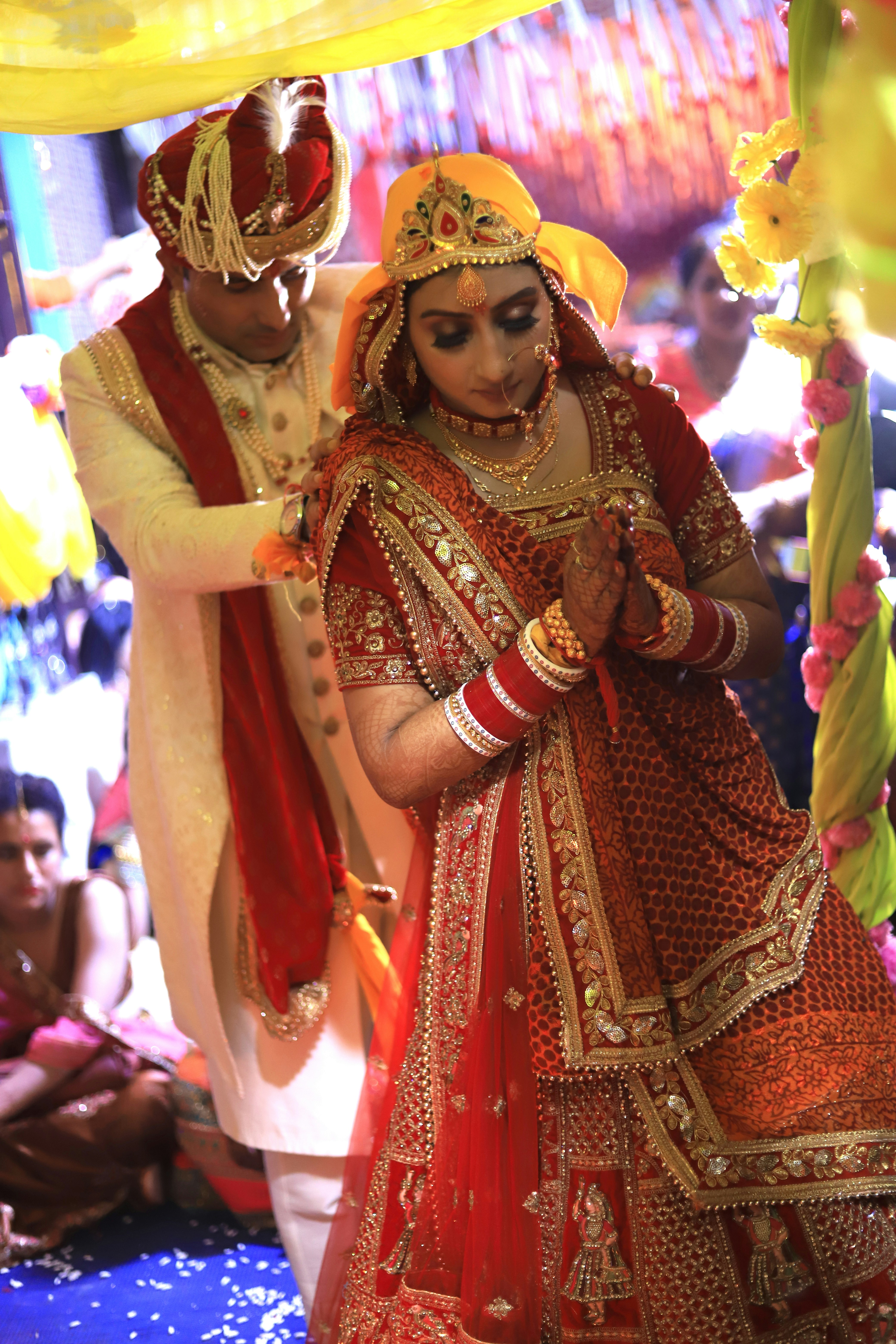 Bride and groom in traditional Indian wedding attire standing in a palace courtyard, golden light, floral garlands