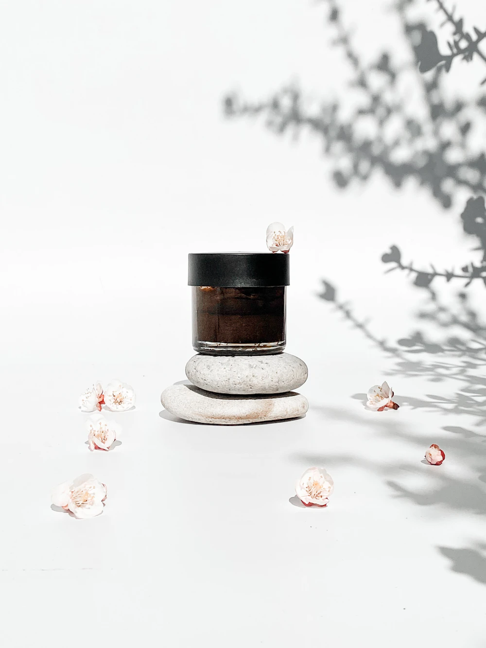 Dark glass cream jar on stones with cherry blossoms