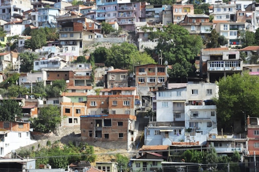 A densely packed hillside with numerous residential houses of various colors and sizes. The buildings are closely clustered together and climb up the slope. Abundant green trees and shrubs are interspersed among the homes, adding natural elements to the urban setting.