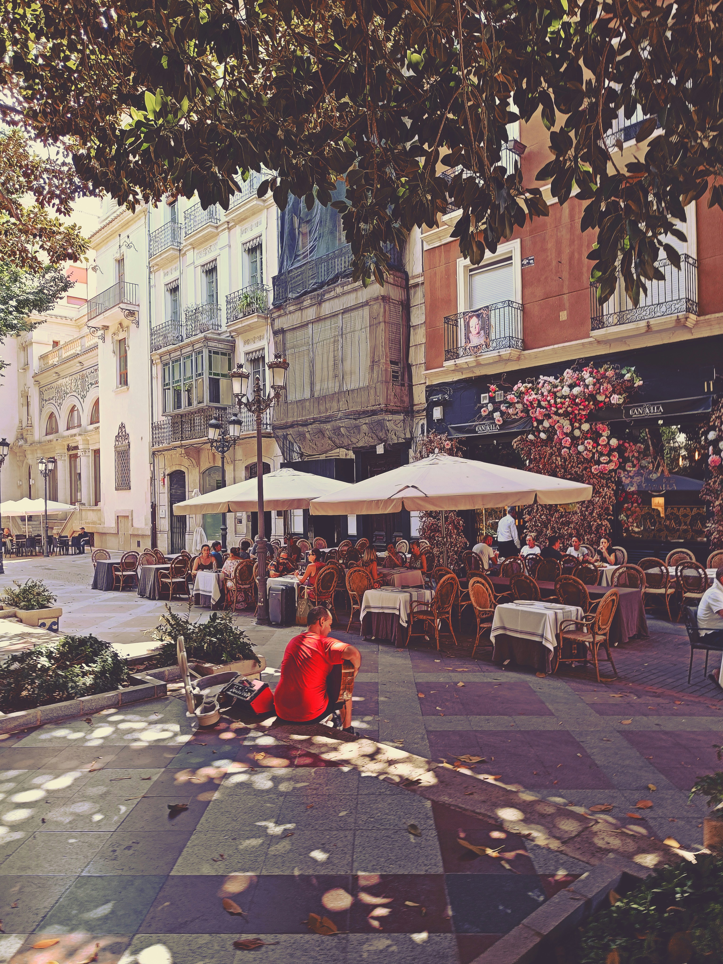 a person sitting on a bench in a courtyard with tables and chairs