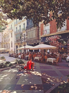 a person sitting on a bench in a courtyard with tables and chairs