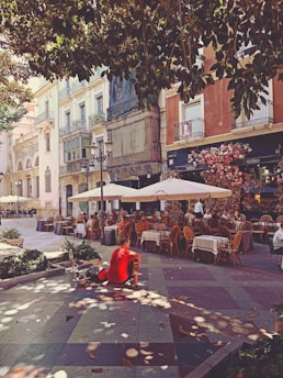 a person sitting on a bench in a courtyard with tables and chairs
