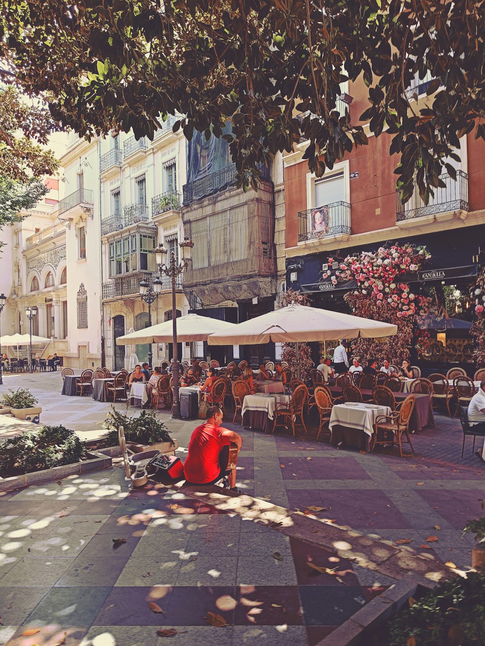 a person sitting on a bench in a courtyard with tables and chairs