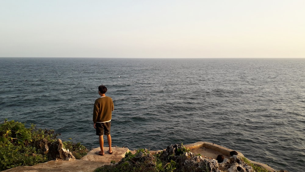 um homem de pé em uma rocha com vista para o oceano