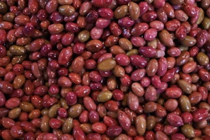 A close-up view of a large quantity of olives, displaying a variety of colors such as red, pink, and green. The olives have a glossy texture, suggesting they are either in brine or oil.