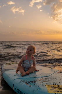 A smiling child sitting on a beach towel, watching the sunset over the ocean