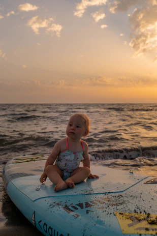 A smiling child sitting on a beach towel, watching the sunset over the ocean