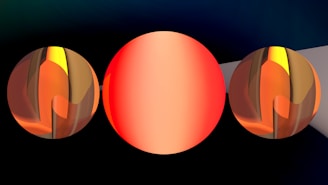 Three abstract spheres with a smooth, reflective surface dominate the image. The central sphere is vivid orange, while the spheres on either side contain swirling patterns of yellows, oranges, and browns. The spheres are set against a dark background, possibly representing space or emptiness.