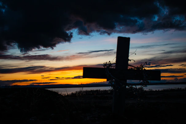 Sunset over a peaceful beach with a cross silhouetted against the sky.