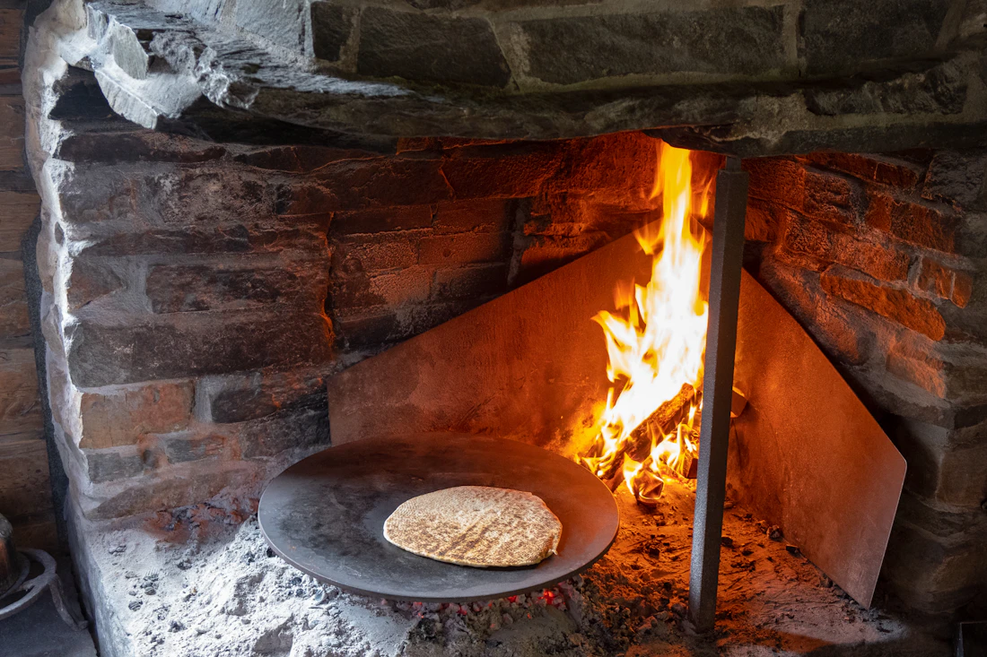 Charcoal glowing inside a brick oven, a flatbread cooking at its mouth