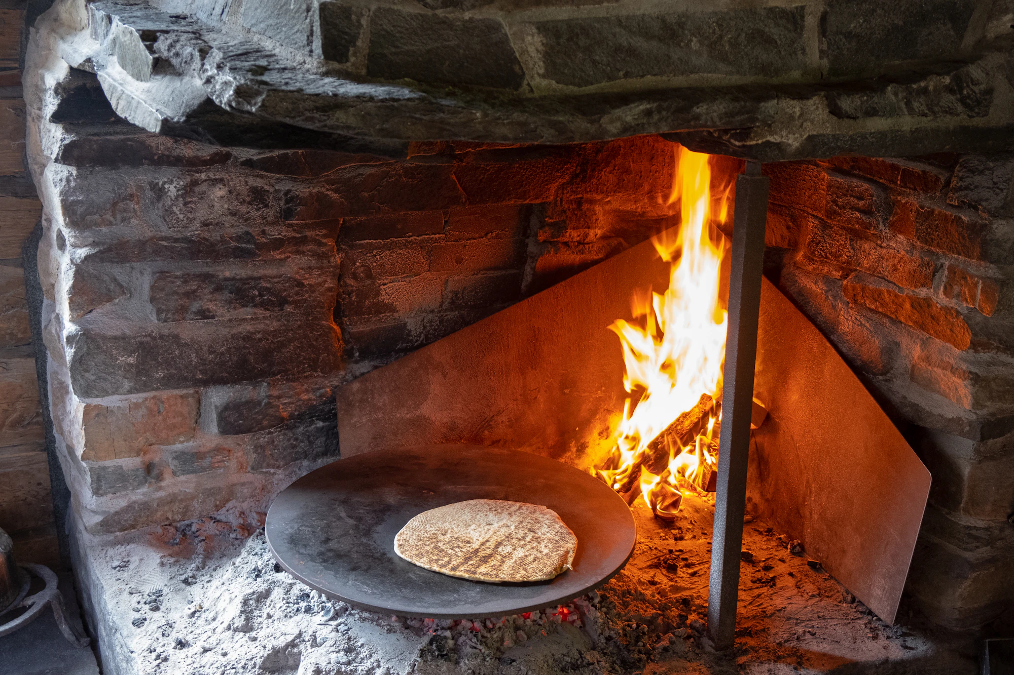 Flames inside a brick oven with a flatbread cooking at its mouth