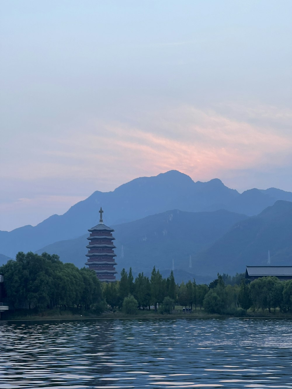 a building next to a body of water with trees and mountains in the background