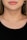A close-up of a woman's neck wearing a simple gold chain necklace. The skin is fair and the lips are in a neutral expression. The woman is wearing an earring with a blue stone on her left ear, and her hair is light brown.