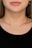 A close-up of a woman's neck wearing a simple gold chain necklace. The skin is fair and the lips are in a neutral expression. The woman is wearing an earring with a blue stone on her left ear, and her hair is light brown.