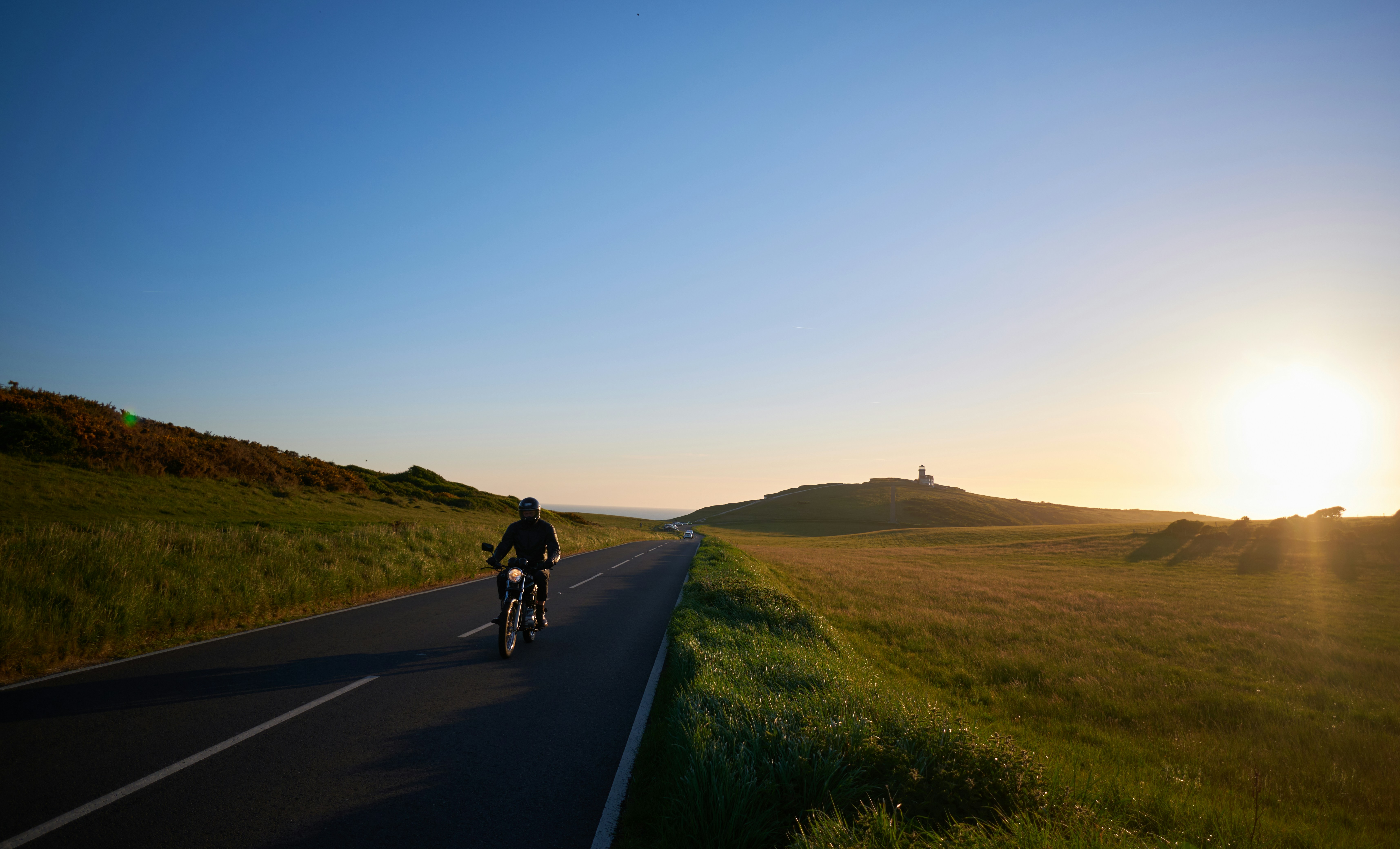 a person riding a bicycle on a road with grass and hills in the background