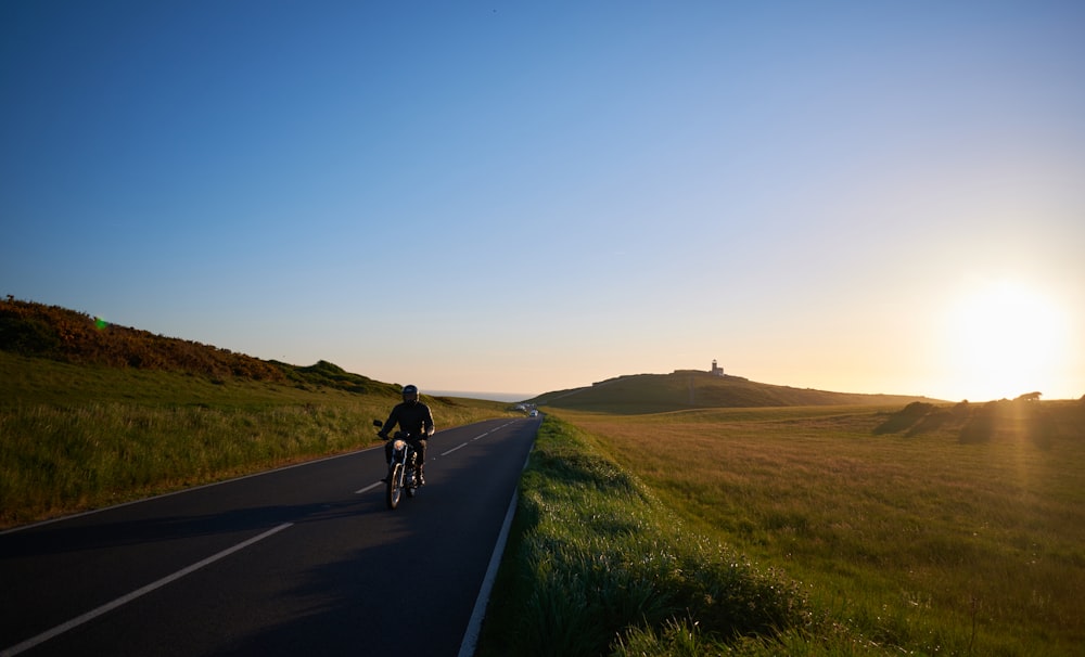 a person riding a bicycle on a road with grass and hills in the background