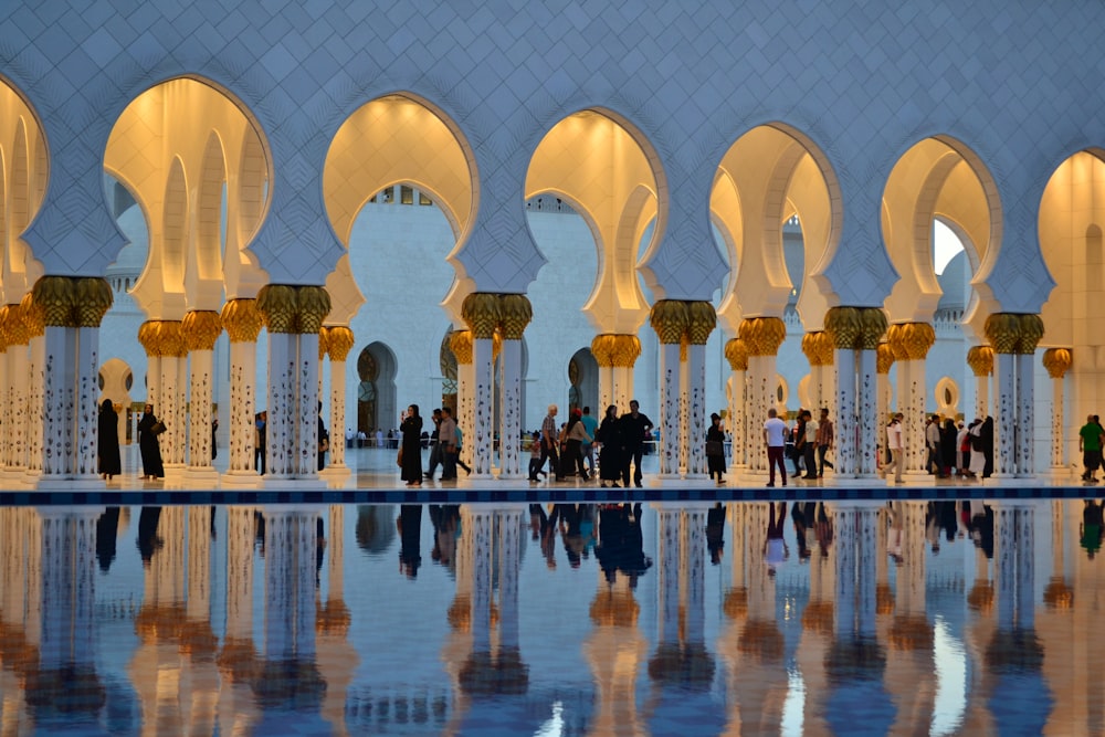 eine Gruppe von Menschen, die in einem großen Gebäude mit Bögen und Säulen mit der Sheikh Zayed Moschee im Hintergrund stehen