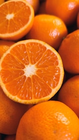 A close-up view of several fresh oranges with one orange cut in half, revealing its juicy segments and vibrant flesh.
