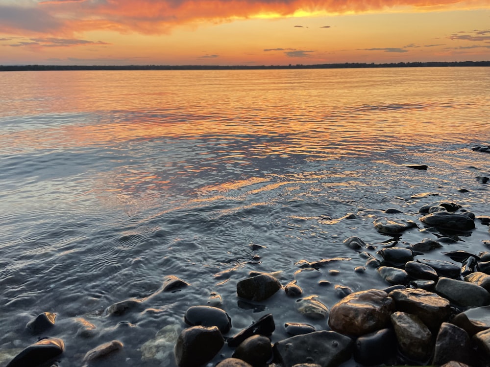 a body of water with rocks in it and a sunset in the background