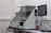 A laboratory machine with a protective transparent cover is positioned on a counter. Next to it, a monitor is attached, and various cables are connected. The setting appears to be sterile, with a focus on technology and instrumentation.