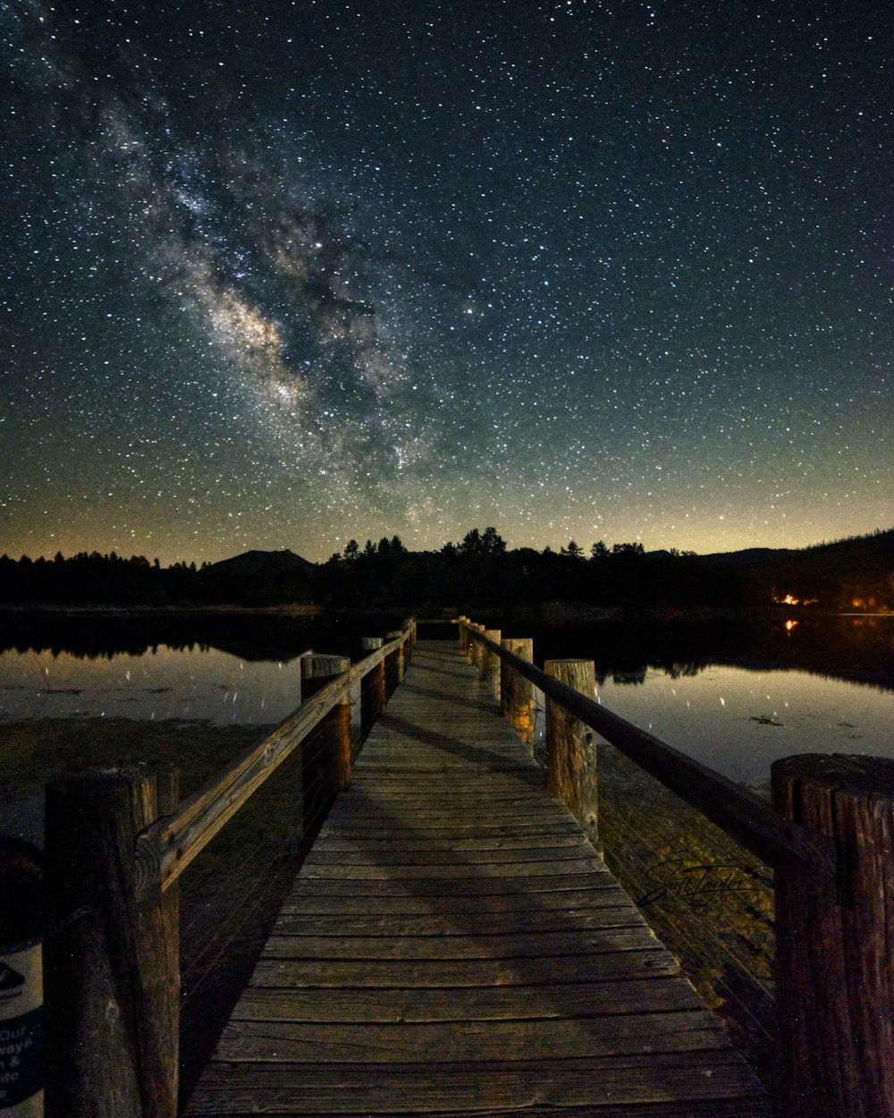 a wooden bridge over water with stars in the sky