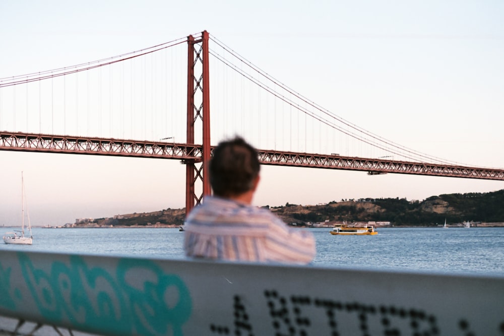 a man sitting on a boat looking at a large bridge