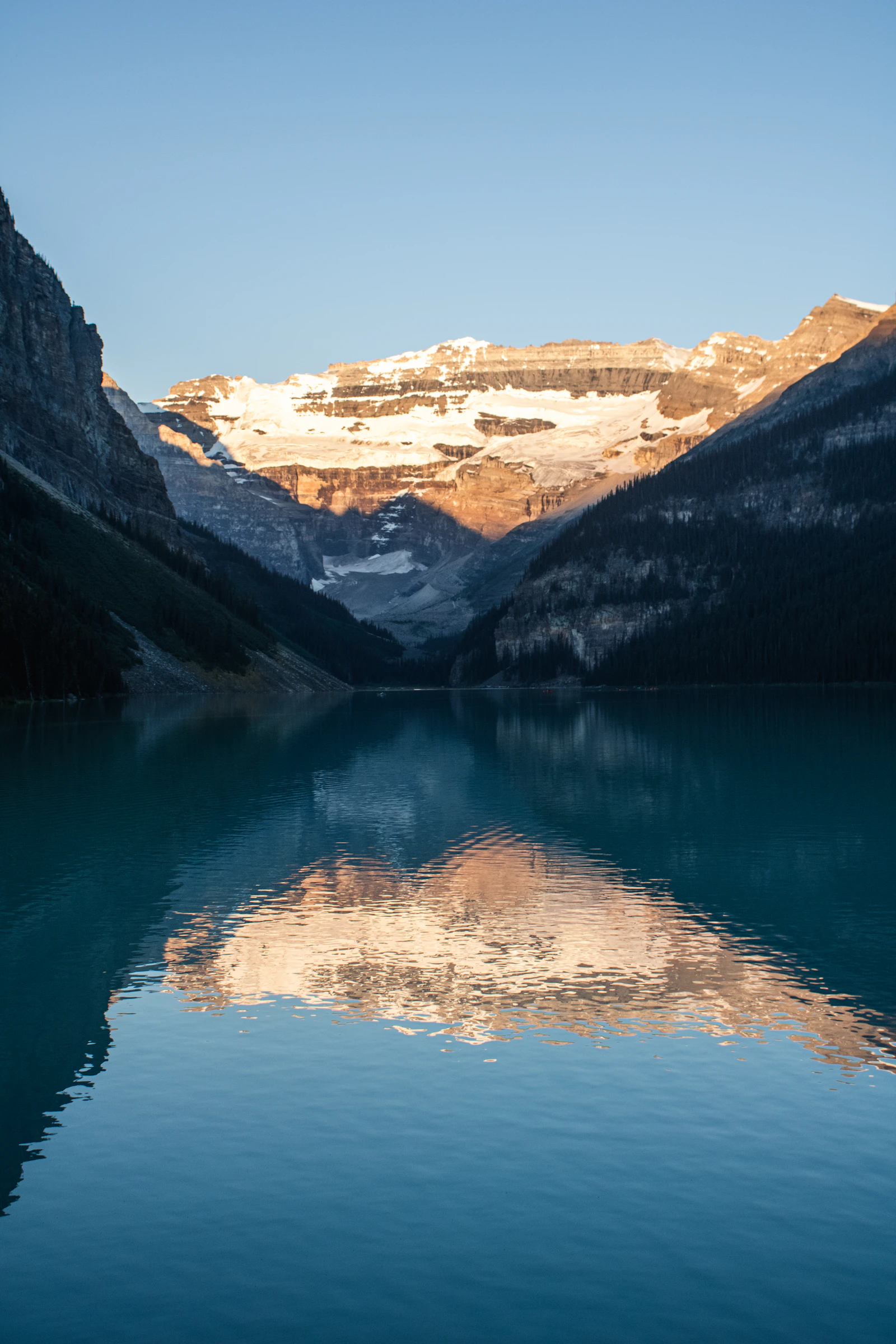 Lake Louise at sunrise with a snow-capped mountain mirrored in still blue Canadian water