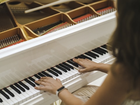 Hands are playing on a white wooden piano, with visible strings and hammers inside the instrument.