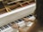 Hands are playing on a white wooden piano, with visible strings and hammers inside the instrument.