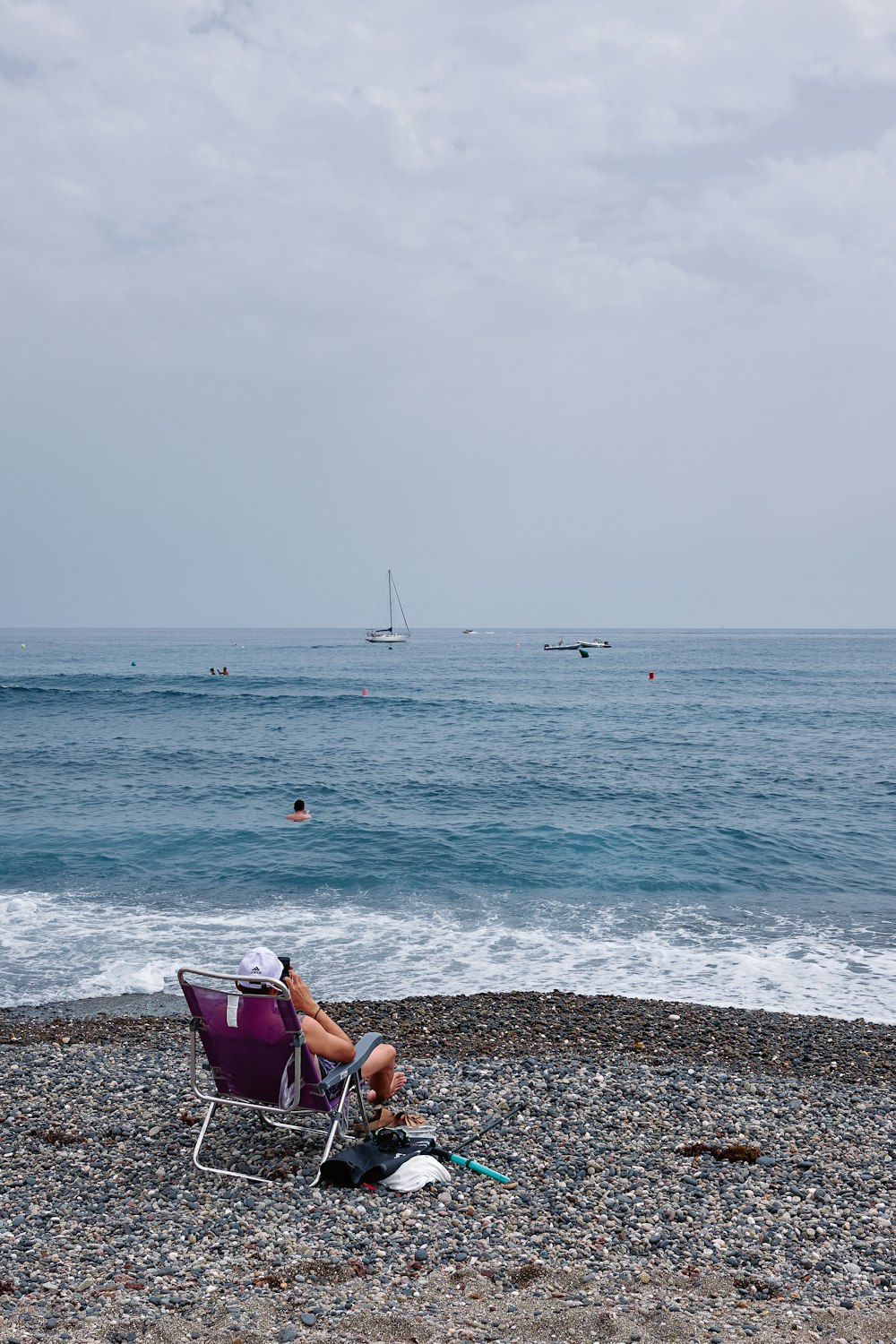 a person sitting in a chair on a beach looking at a sailboat