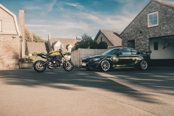 A sleek motorcycle parked beside a shiny sports car under a clear blue sky.