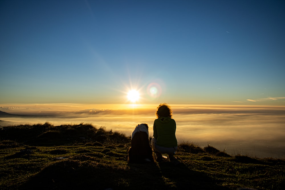 a couple of people sitting on a hill looking at the sun