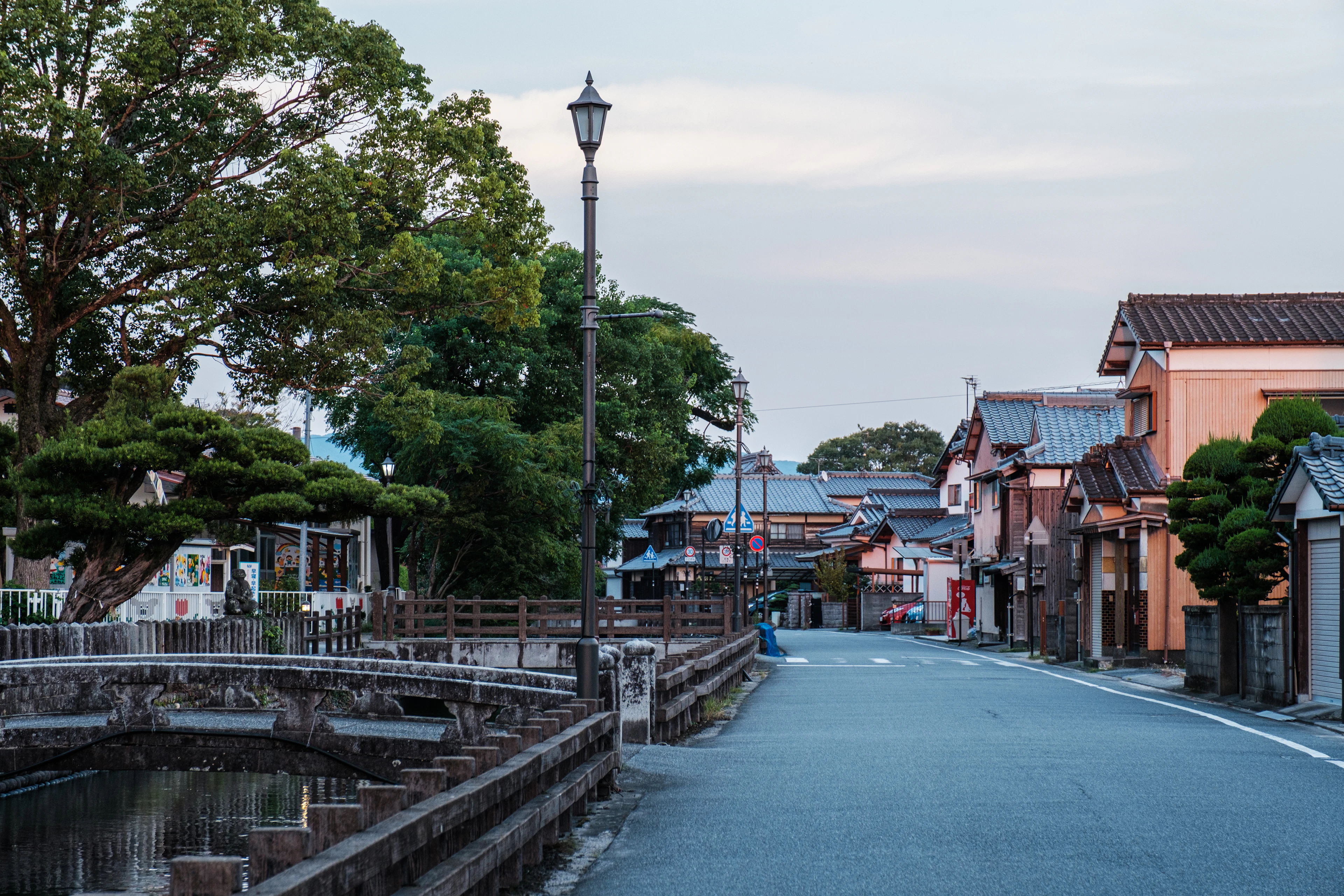 A quiet lamplit street lined with old wooden buildings runs beside a canal at dusk.