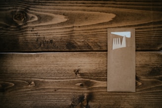 A wooden surface with a brown envelope containing a plastic fork and a white napkin.