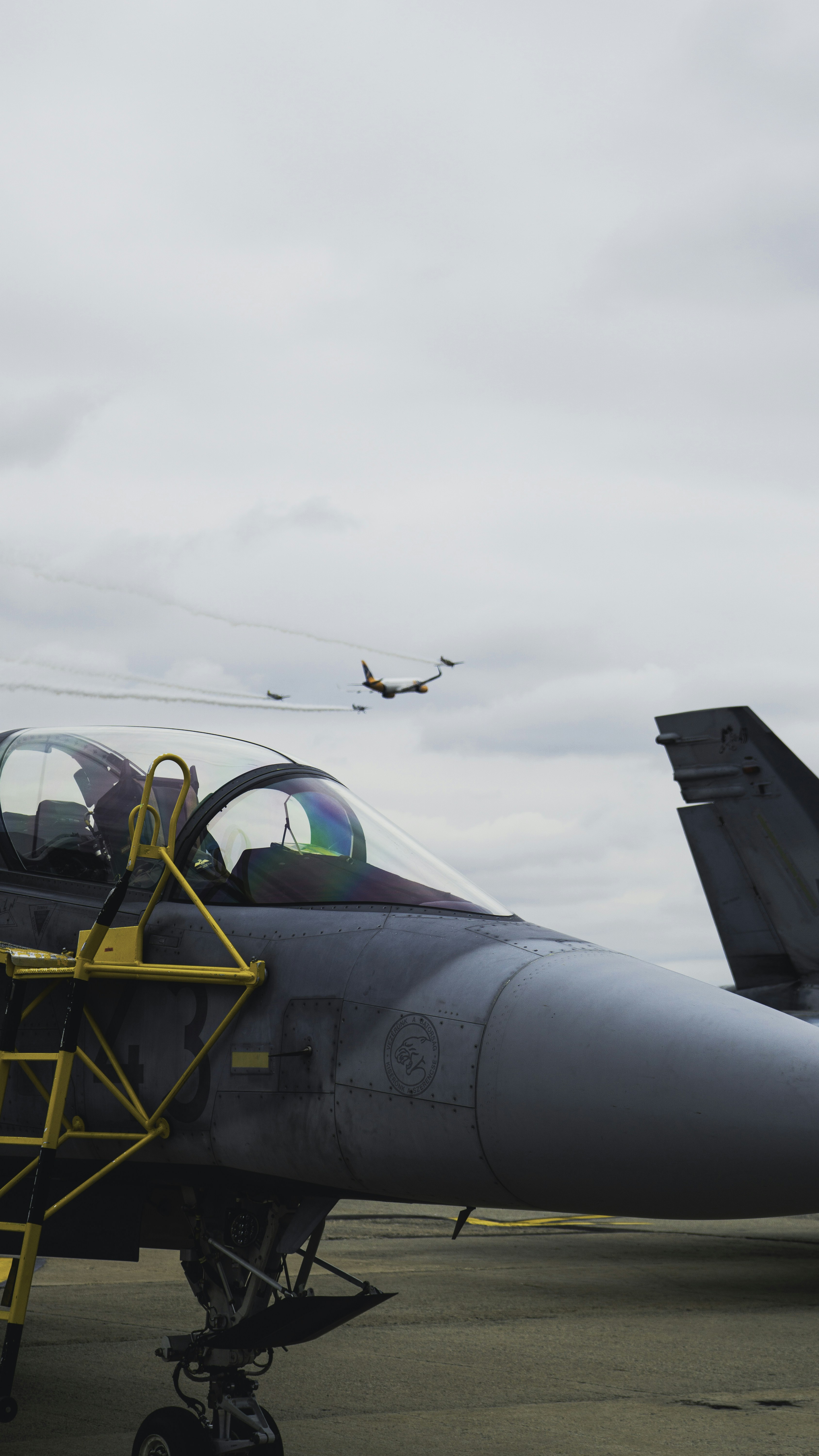 Kampfjet auf Rollfeld mit Flugzeugen, die darüber fliegen