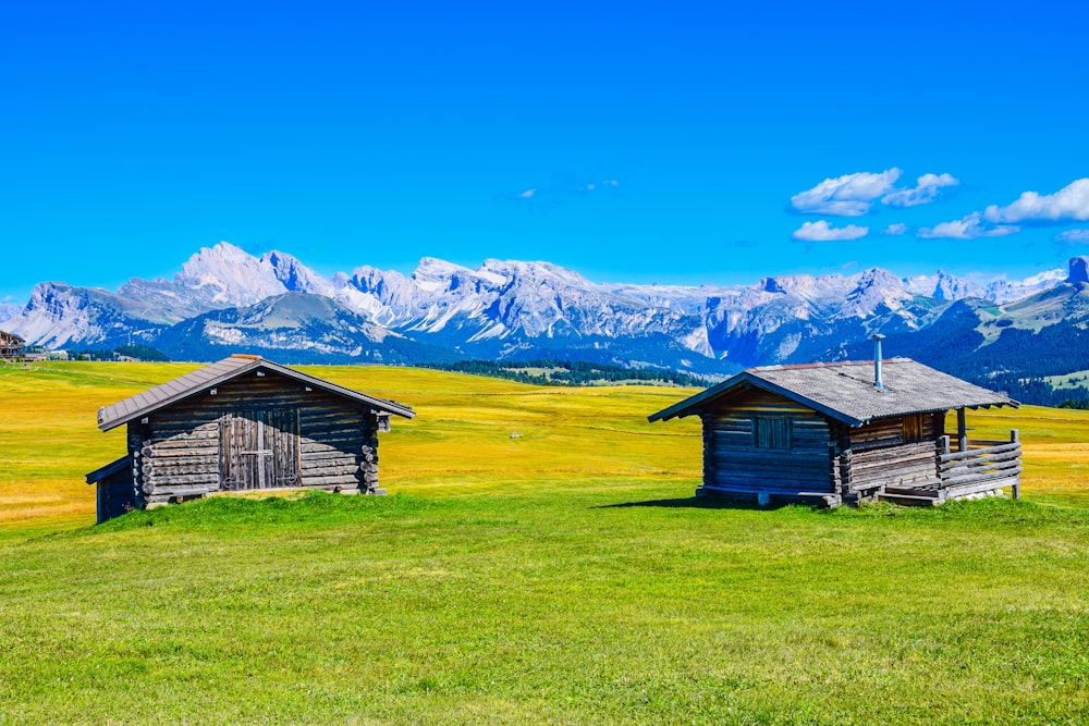 a couple of small buildings in a grassy field with mountains in the background