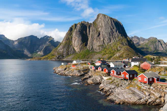 a group of houses by a body of water with mountains in the background with Lofoten in the background