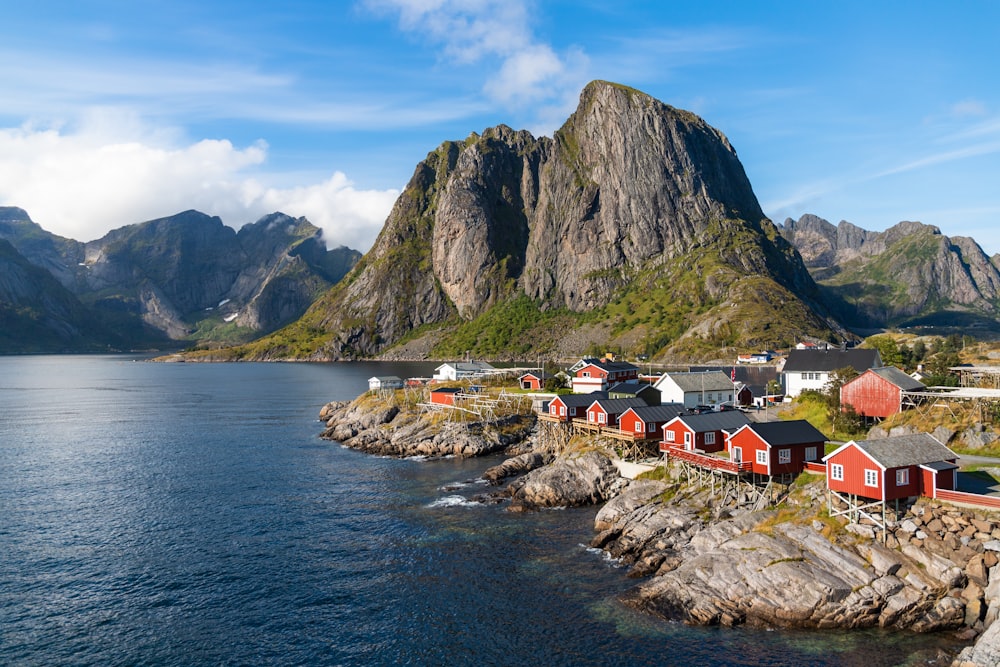 un gruppo di case vicino a uno specchio d'acqua con le montagne sullo sfondo con le Lofoten sullo sfondo