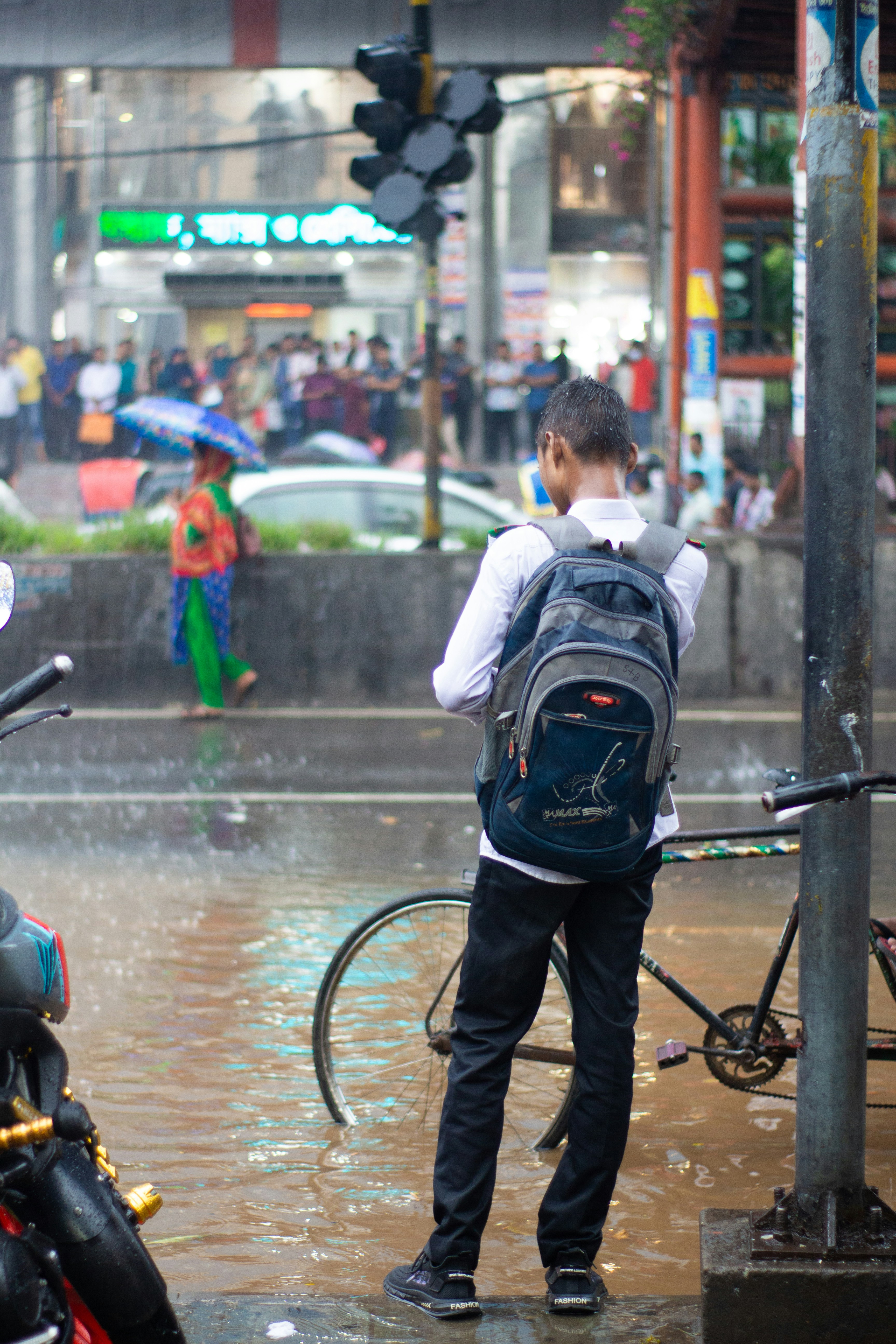 a man with a backpack standing on a sidewalk in the rain