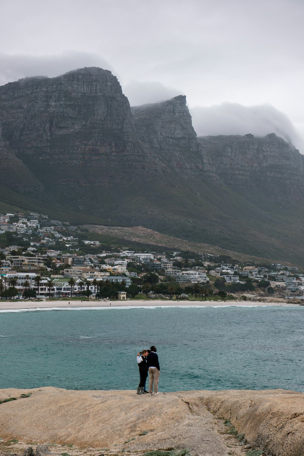 a couple kissing on a cliff by a body of water and mountains