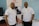Two men wearing white polo shirts with a logo stand in front of a banner. The banner displays the name 'Inkanyeti Foundation' and an image of a person with glasses. There is a table with items in the background to the right.