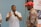 A man in a white polo shirt is gesturing with his hands while speaking to an older man wearing a red cap and a floral shirt. A partially visible person stands to the side. A banner from the Inkanyezi Foundation is displayed in the background.